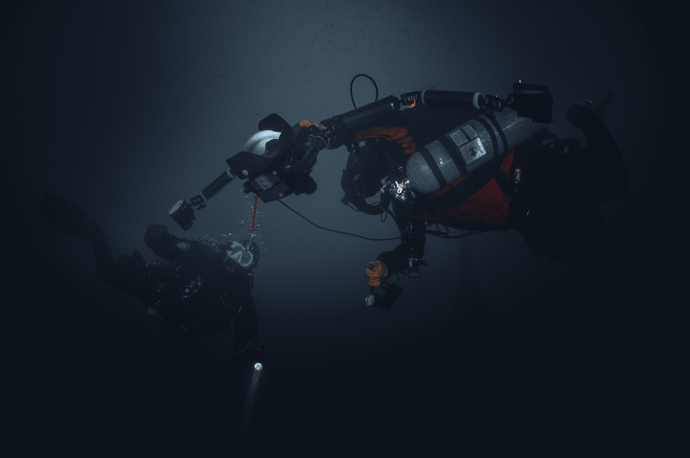 Two divers in dark water, one lining up a camera rig with a strobe