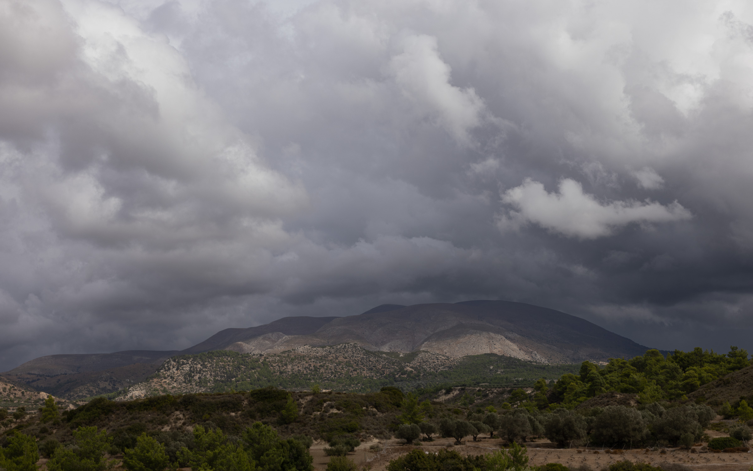 Heavy storm clouds building over a mountain and olive groves